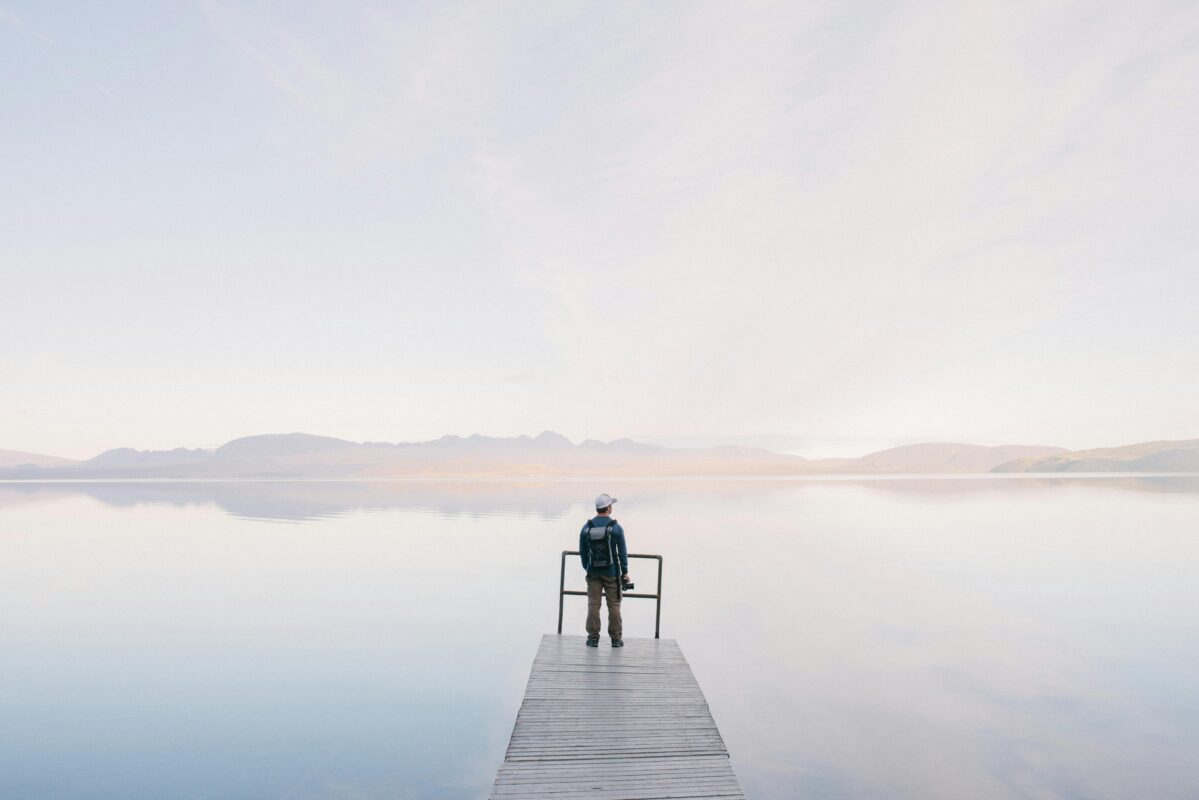 A solitary traveler stands on a dock enjoying the serene water view